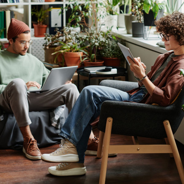 Two young serious coworkers using wireless mobile gadgets Two young serious coworkers using wireless mobile gadgets while sitting in armchairs in openspace office with variety og green plants